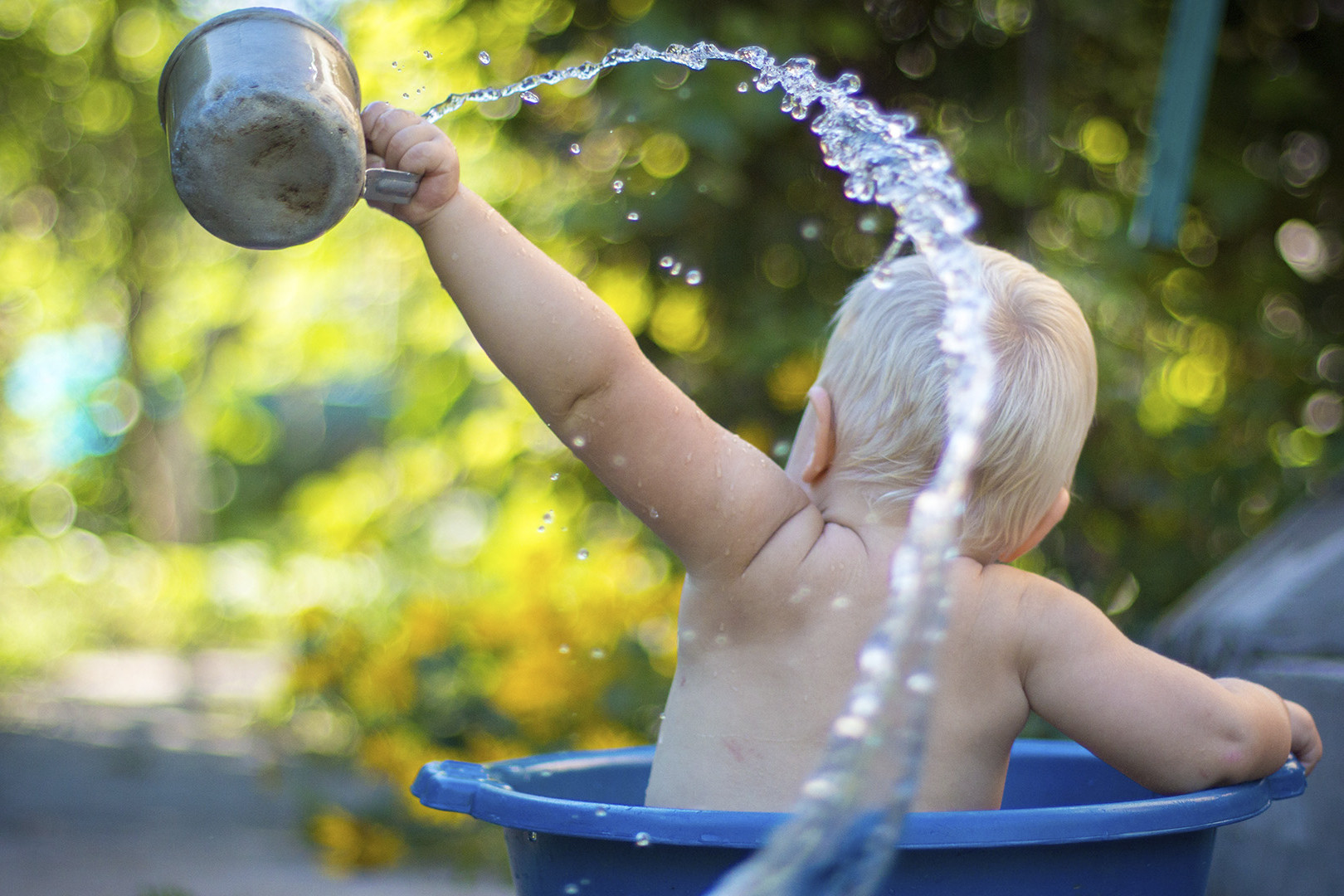 Lapsi kylpe pesuvadissa, heittää kupilla vettä