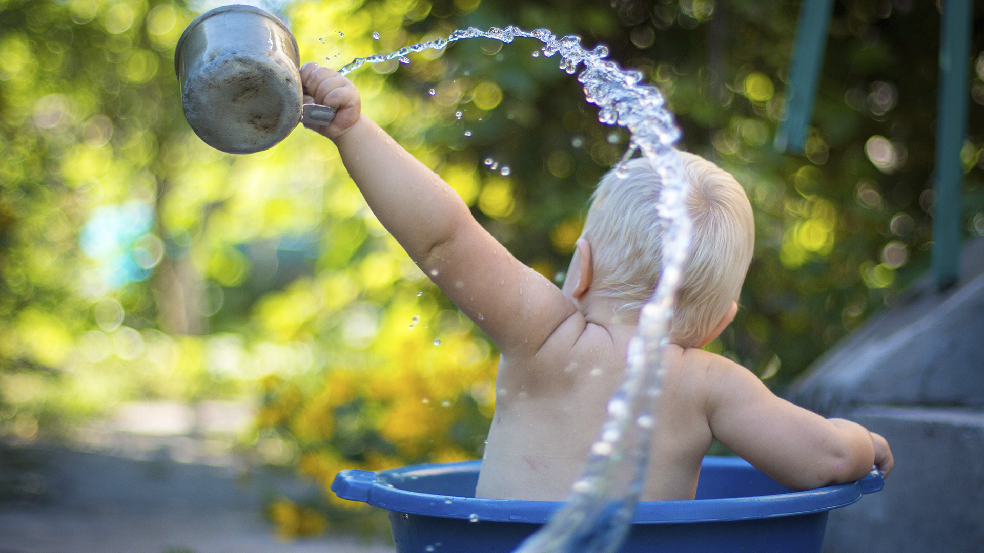 Lapsi kylpe pesuvadissa, heittää kupilla vettä.