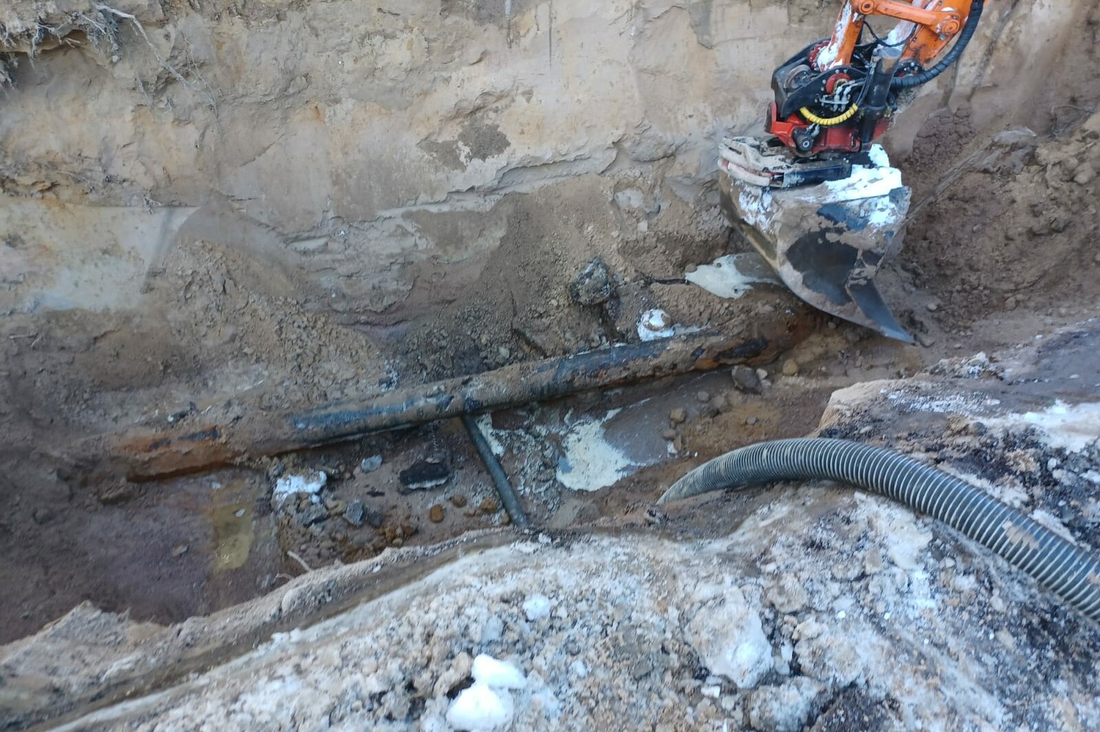 kauhakuormaajan kauha kaivaa monttua saadakseen rikkoutuneen vesiputken esiin maan alta