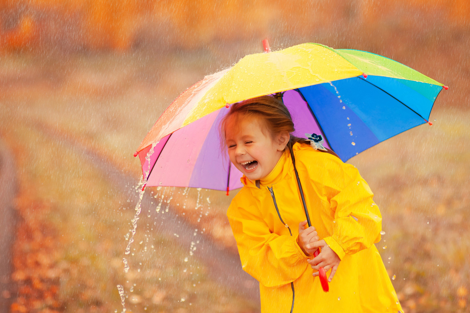 Tyttö nauraa vesisateessa sateenvarjon kanssa