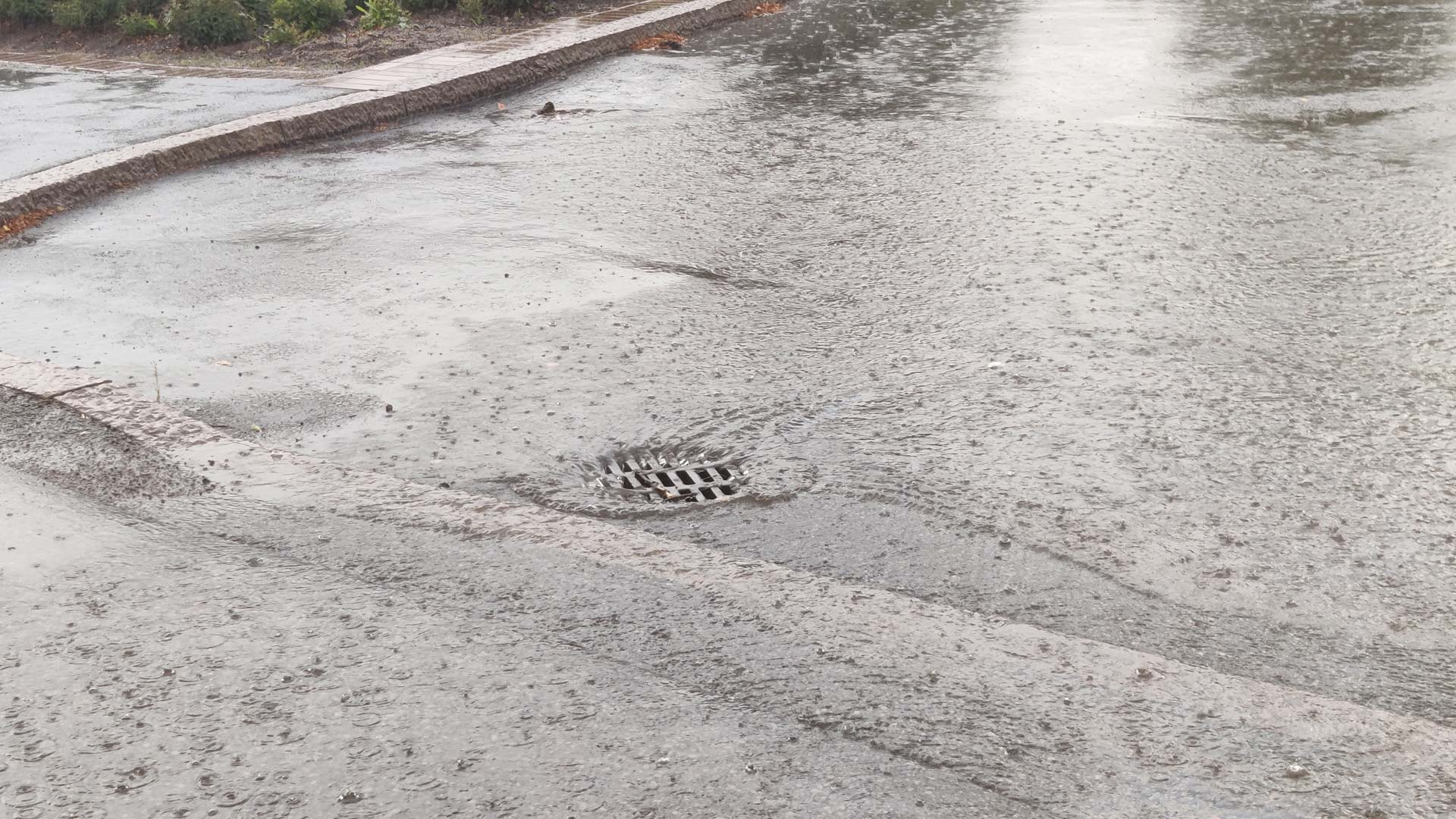 Kuvassa kadulla sadevettä joka valuu ritiläkaivoon.